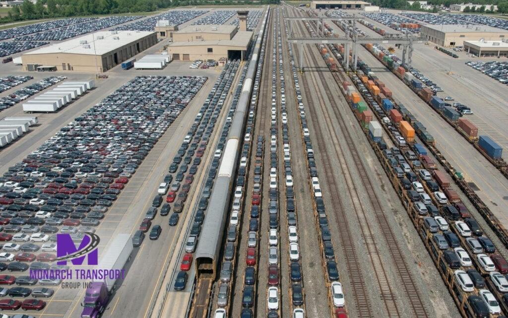 Monarch - Car Shipping by Train (4) Large rail yard with vehicles prepared for train shipping and logistics truck